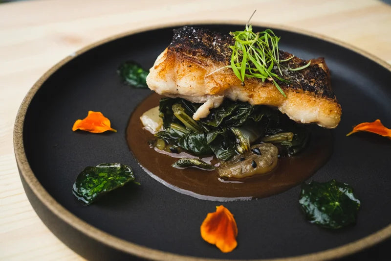 Fish with vegetables and sauce on a dark plate