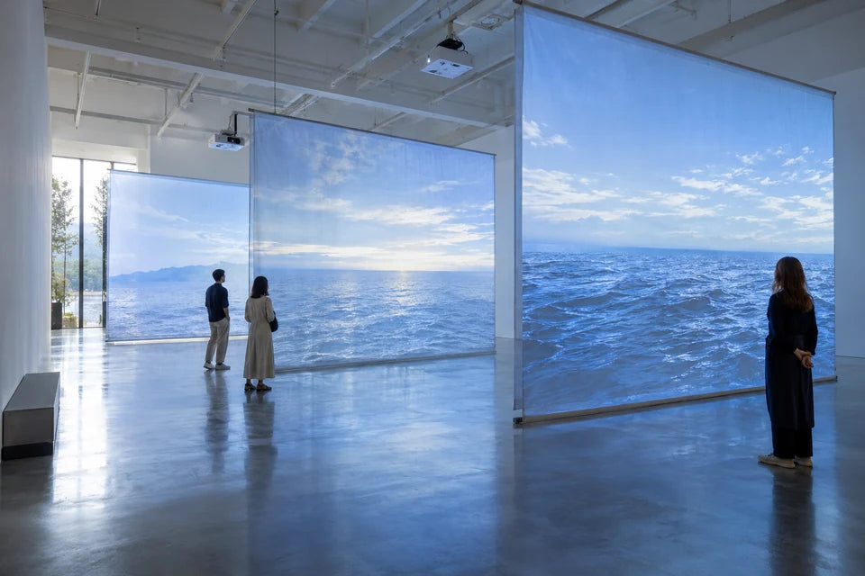 Visitors explore a gallery installation of large suspended ocean-projection screens.